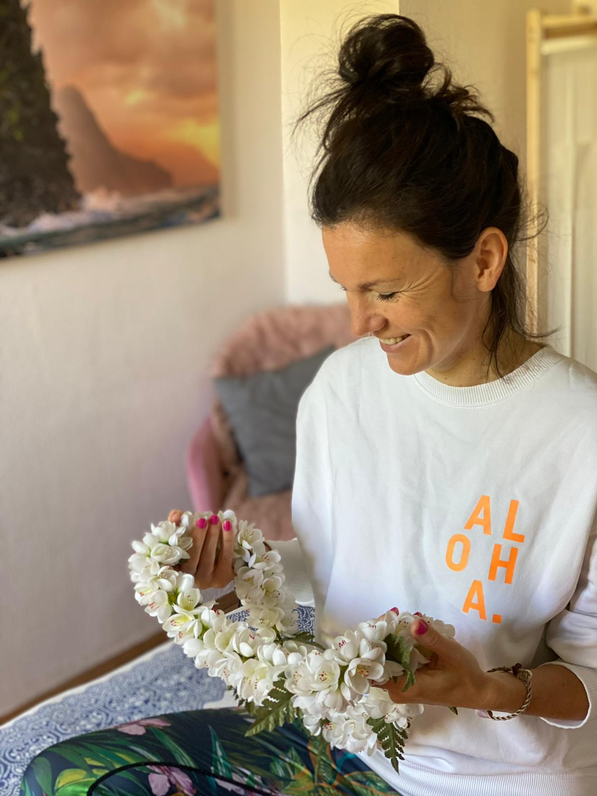 Eine Frau sitzt auf einem Bett, umgeben von bunten Blumen, die eine fröhliche und entspannte Atmosphäre schaffen.